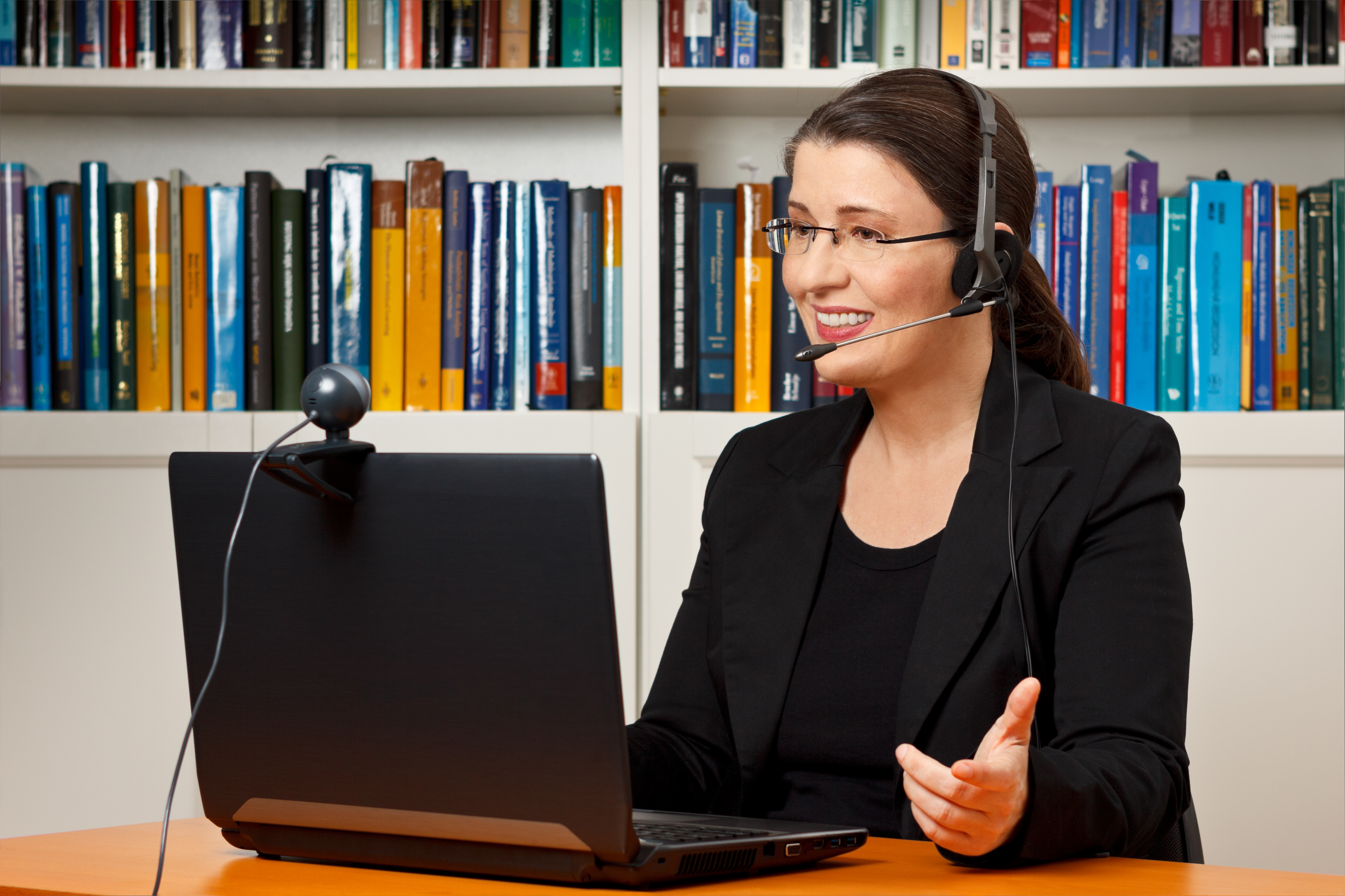 Teacher, tutor or professor with headset, laptop and camera in her office explaining something at an online lesson or video lecture, webinar