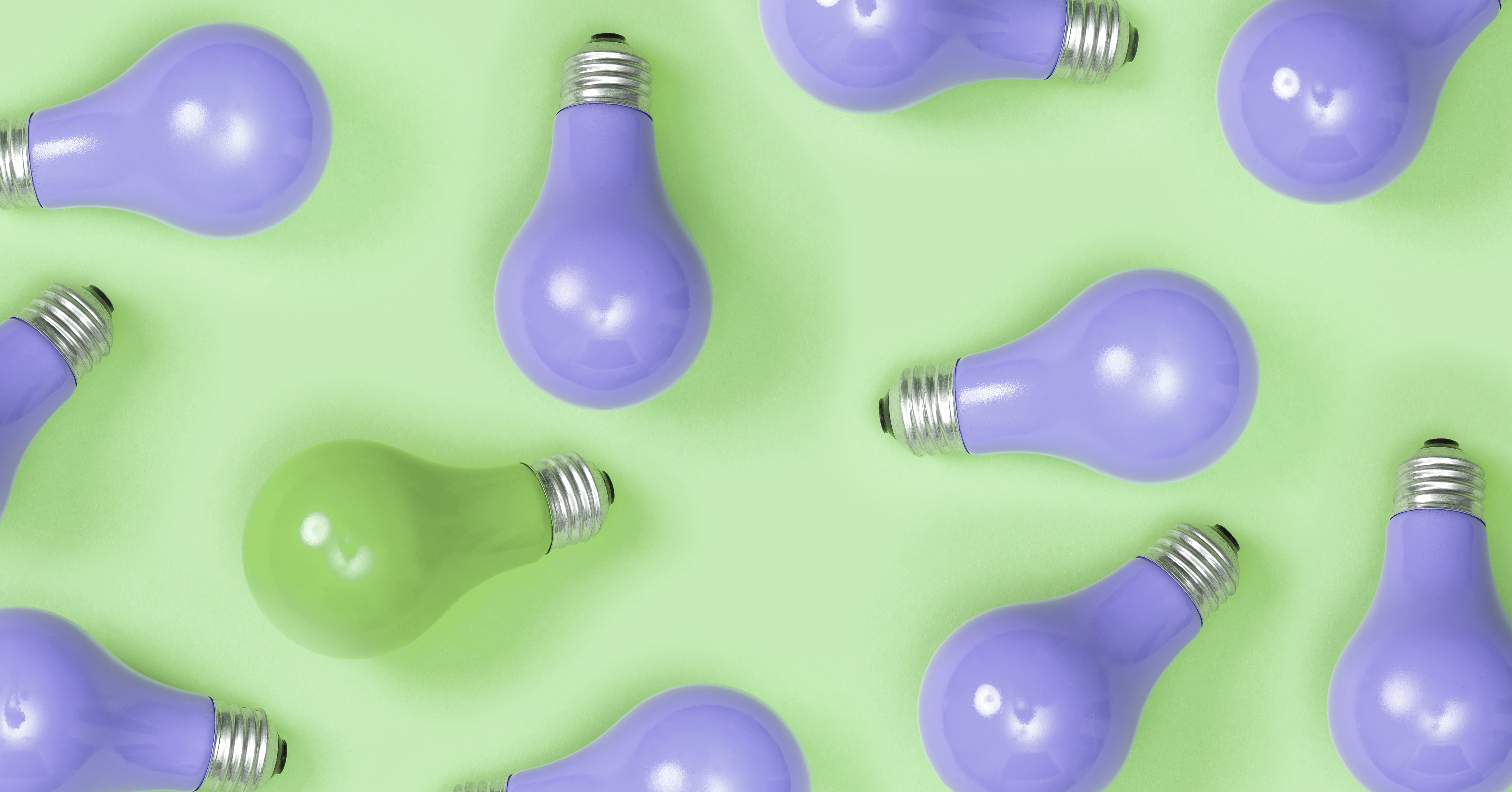 Purple painted lightbulbs on a green background, wil one green