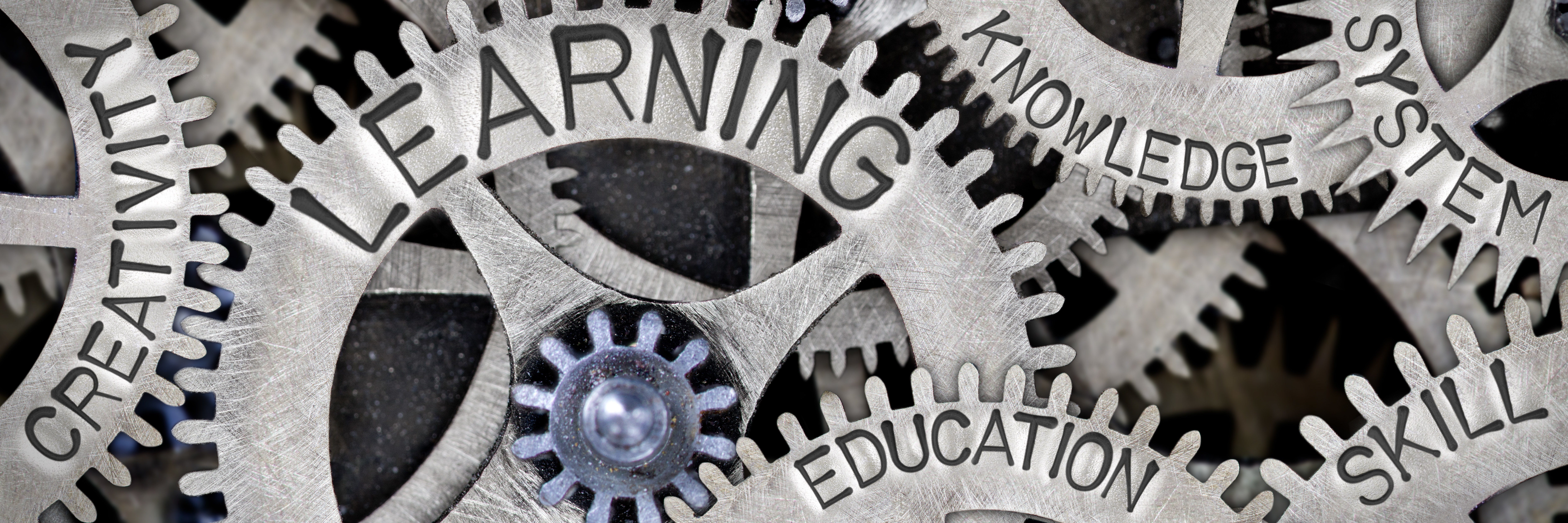 Metal Wheel Concept Macro photo of tooth wheel mechanism with LEARNING, CREATIVITY, EDUCATION, SKILL, SYSTEM and KNOWLEDGE words imprinted on metal surface